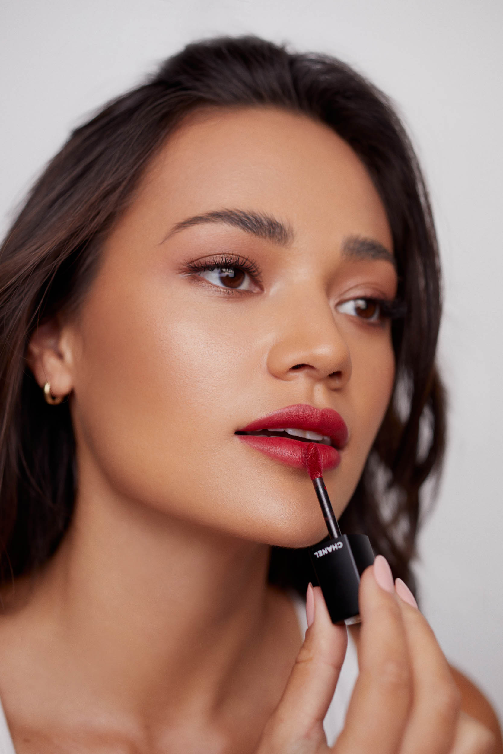 Portrait of a woman applying red lipstick in a bright, indoor studio setting. Close-up shot emphasizes cosmetic details.