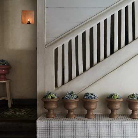 Interior view of a staircase with white banisters, accompanied by a row of terracotta pots filled with plants on a tiled surface.