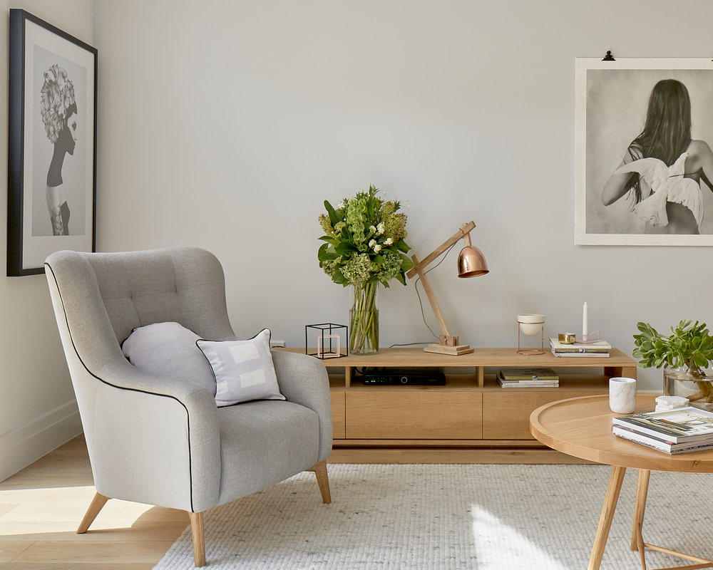 Modern living room interior with a gray armchair, wooden console table with flowers, and a round coffee table on a light rug.