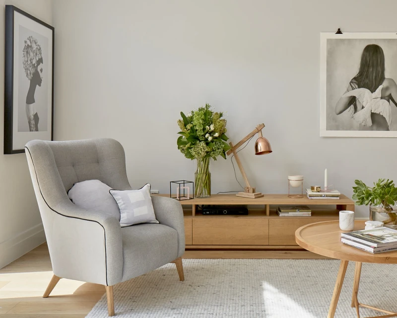 Modern living room interior with a gray armchair, wooden console table with flowers, and a round coffee table on a light rug.
