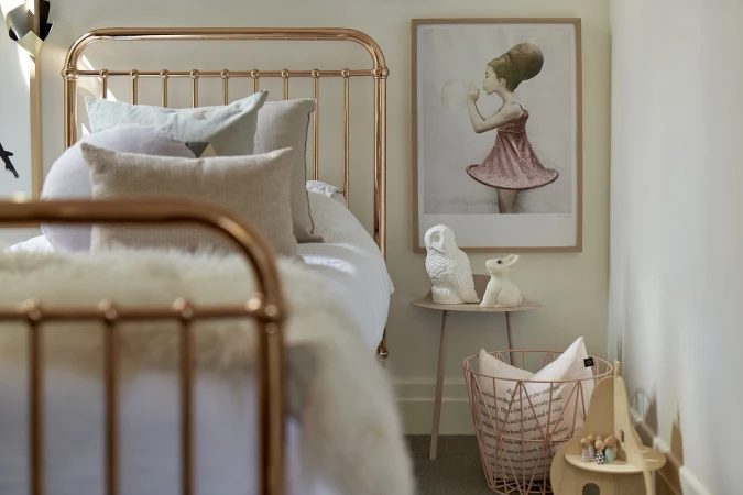 Bedroom interior featuring a bronze metal bed frame, various pillows, and a framed illustration of a girl blowing bubbles on the wall.