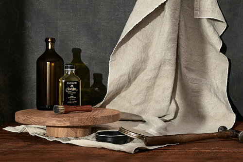 Still life of shoe cleaning and care products including polish, brush, oil and cloth arranged on a wooden surface against a dark background.