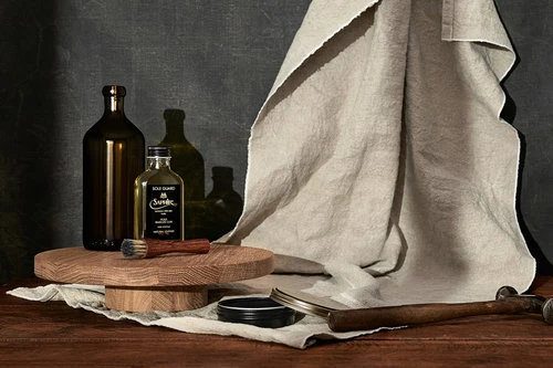 Still life of shoe cleaning and care products including polish, brush, oil and cloth arranged on a wooden surface against a dark background.
