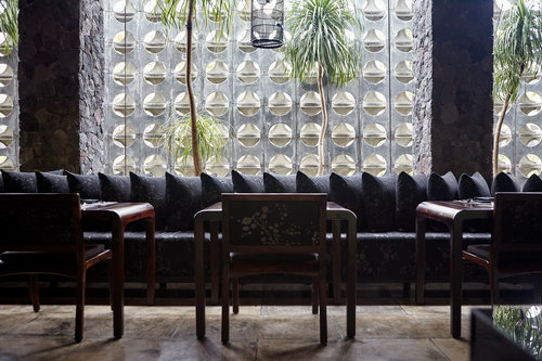 Stylish restaurant interior featuring dark wood furniture, cushioned seating, and a textured wall with geometric patterns and natural light.