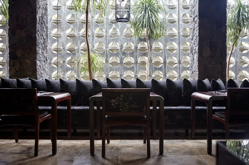 Stylish restaurant interior featuring dark wood furniture, cushioned seating, and a textured wall with geometric patterns and natural light.
