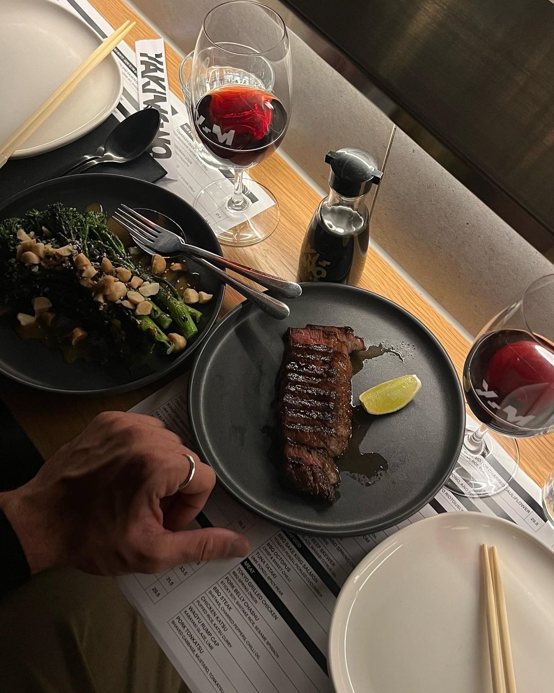 Overhead shot of a restaurant table with steak, greens, wine, and a hand, highlighting a fine dining experience.