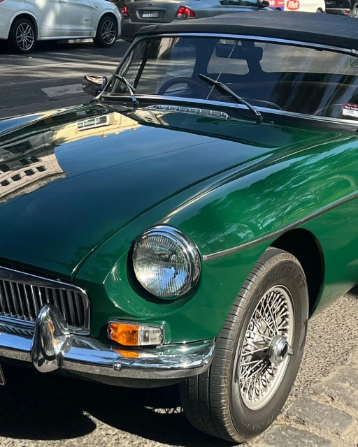 Close-up of a vintage green MGB convertible car parked on a cobblestone street, showcasing its chrome details and wire wheels.