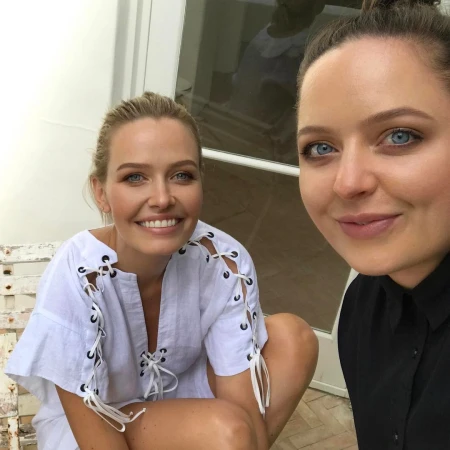 Two women posing together, one wearing a white lace-up top and the other in a black button-down shirt outdoors in Sydney.