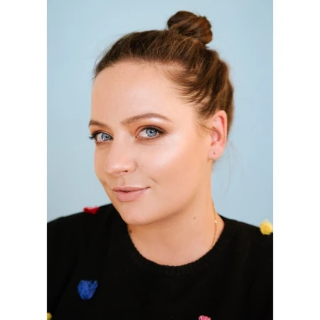 Close-up portrait of a woman with a top knot hairstyle wearing a black sweater against a light blue background.