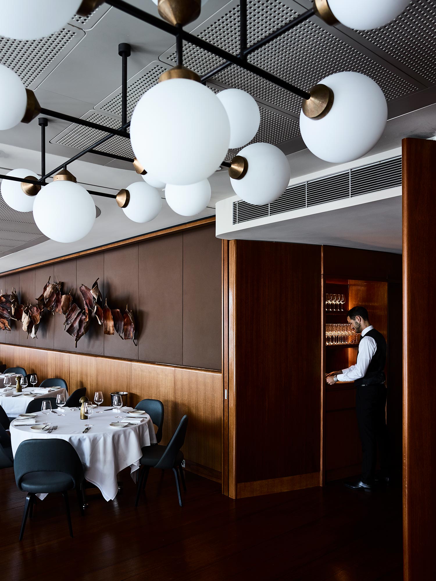 A restaurant interior view showing tables set for dining, globe lighting fixtures, and a server near a doorway.