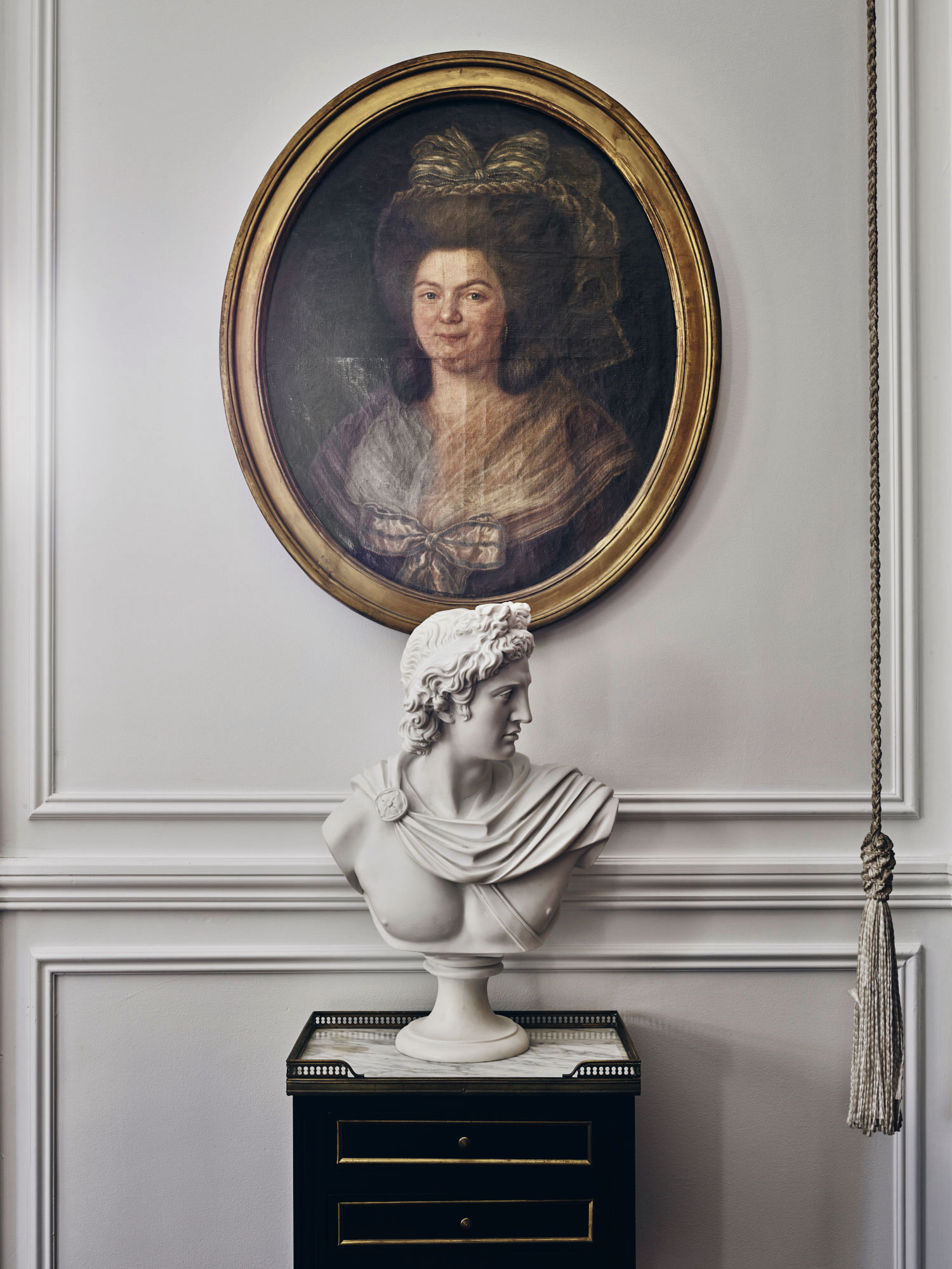 Interior view featuring a bust atop a black cabinet, an oval portrait of a woman, and neutral tones, creating a classic, elegant ambiance.