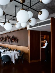 Restaurant interior with globe pendant lights, set dining tables, and a waiter organizing glassware in Sydney by Anson Smart