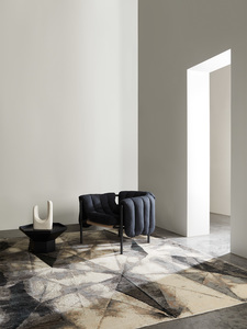 Interior design featuring a blue armchair, a black side table with a white sculpture, and a geometric patterned rug in a well-lit space.