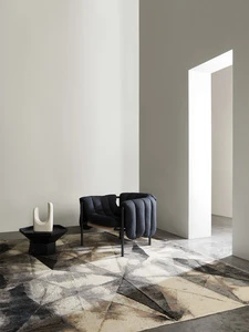 Interior design featuring a blue armchair, a black side table with a white sculpture, and a geometric patterned rug in a well-lit space.