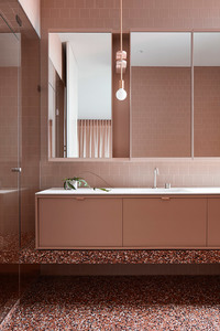 Bathroom interior featuring a vanity with a white countertop, light pink cabinets, pink-tiled wall, mirror, and terrazzo flooring.