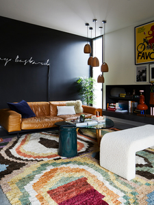 Living room interior with a brown leather sofa, colorful rug, decorative objects, and art against a dark gray wall.
