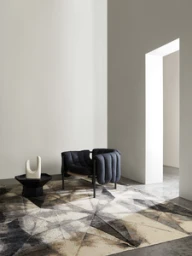 Modern dark upholstered armchair on a patterned geometric rug with a small black side table and white ceramic sculpture