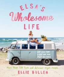 Woman sitting atop a light blue and white vintage camper van parked near a sandy beach with the ocean in the background