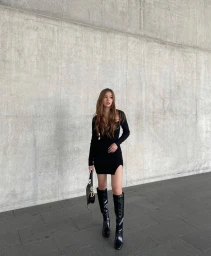 Content creator Ashleigh Huynh in a black dress and boots standing against a concrete wall