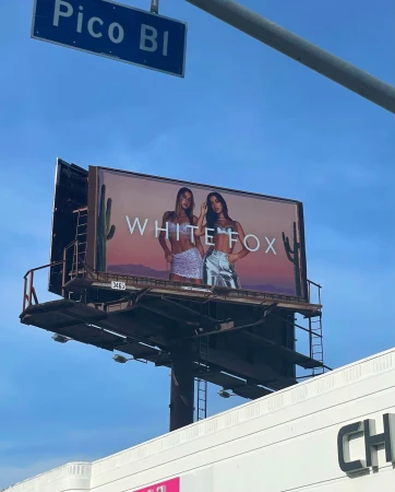 Outdoor billboard advertisement for White Fox featuring two female models against a desert backdrop beneath a blue sky.