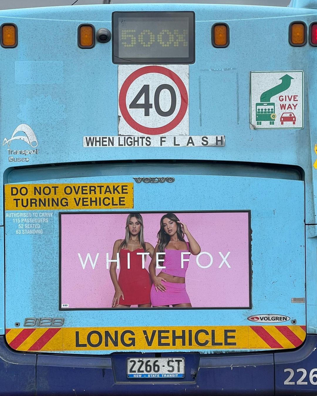Bus exterior showing an ad for White Fox featuring two adult women, wearing pink and red outfits, against a light blue background.