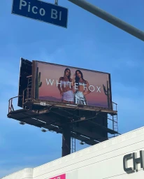 Outdoor billboard advertisement for White Fox featuring two female models against a desert backdrop beneath a blue sky.
