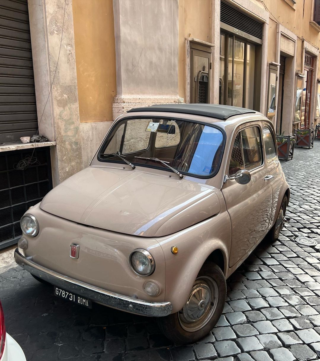 Beige vintage Fiat car parked on a cobblestone street in Rome, Italy, showcasing classic automotive design and urban charm.