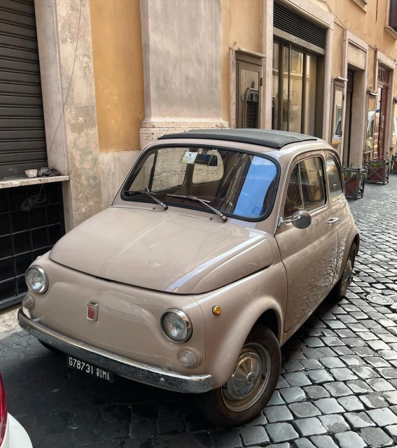 Beige vintage Fiat car parked on a cobblestone street in Rome, Italy, showcasing classic automotive design and urban charm.