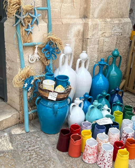 Colorful handcrafted pottery and decorative sea-themed ornaments are displayed outside on a stone surface in a market setting.