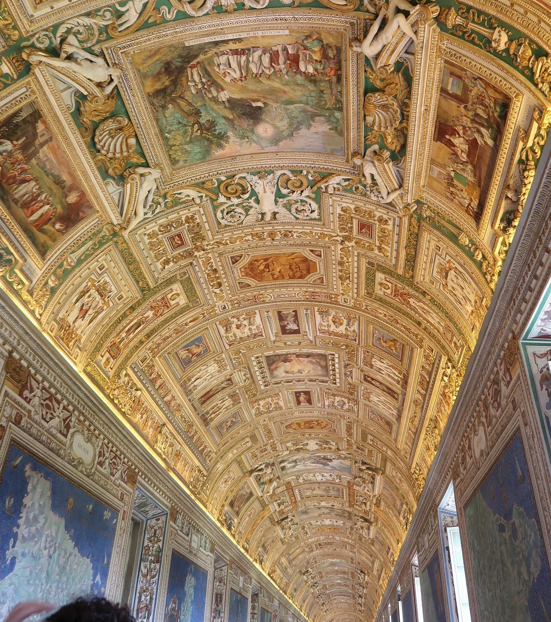 Ornate ceiling with paintings and sculptures in a grand hall, featuring intricate architectural details and artistic embellishments.
