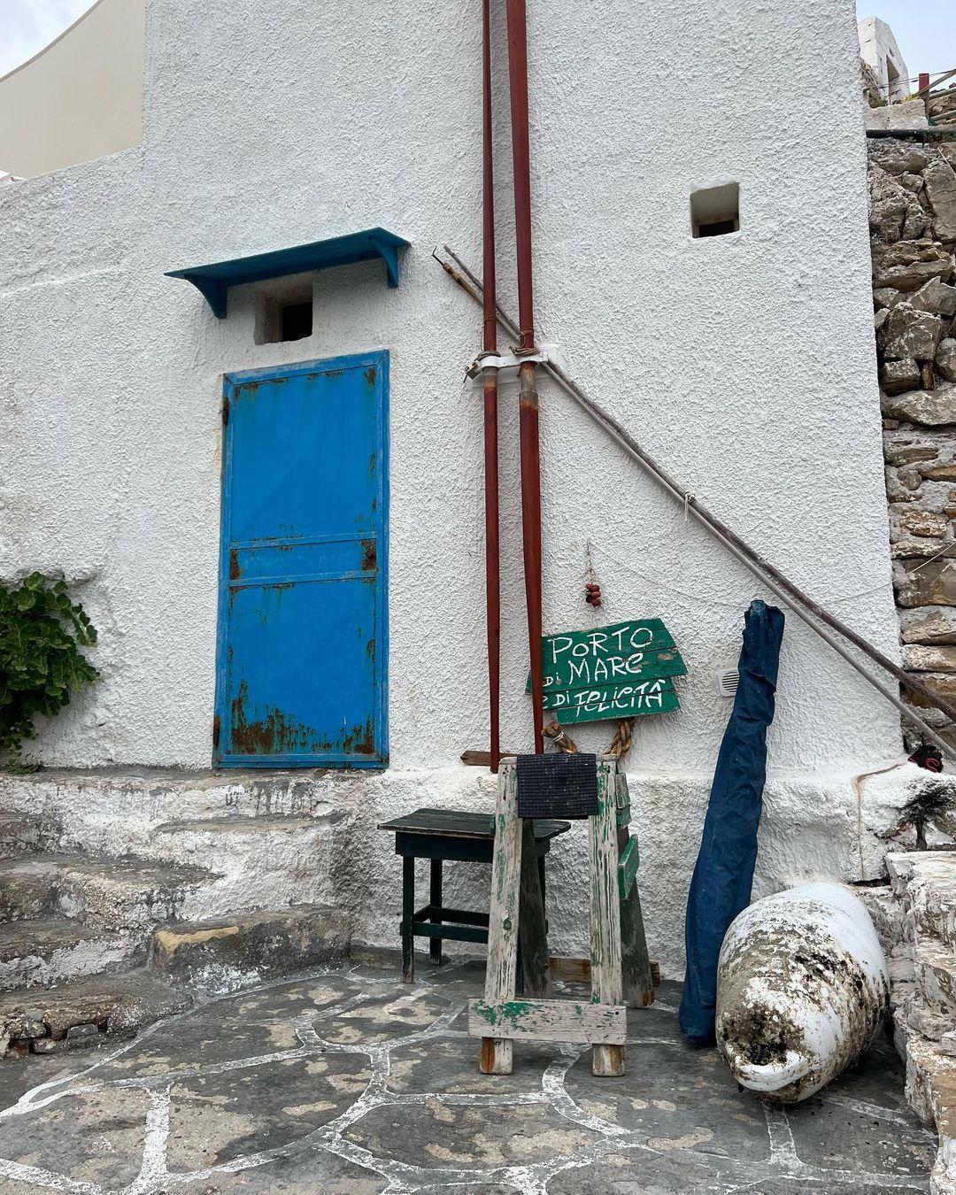 Outdoor scene showcases a weathered blue door of a white building with adjacent objects, creating a rustic, charming Mediterranean vibe.