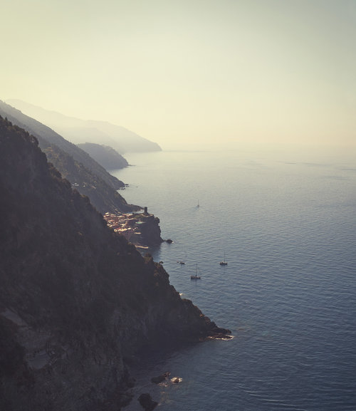 Coastal vista with the Cinque Terre village on a cliff, overlooking the Mediterranean Sea, with boats dotting the calm waters at daylight.