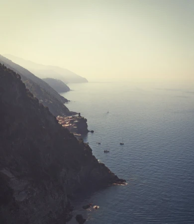 Coastal vista with the Cinque Terre village on a cliff, overlooking the Mediterranean Sea, with boats dotting the calm waters at daylight.