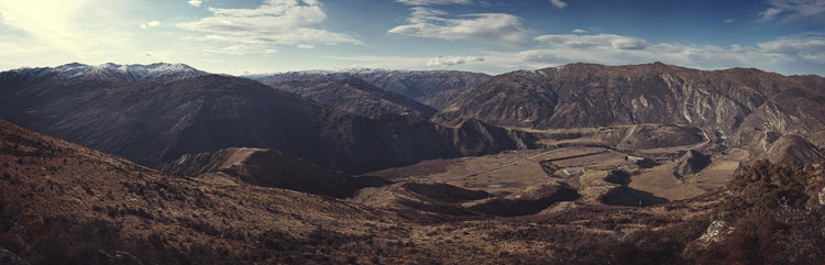Panoramic shot of a vast mountain range with snow-capped peaks under a partly cloudy sky, highlighting the rugged landscape and natural beauty.