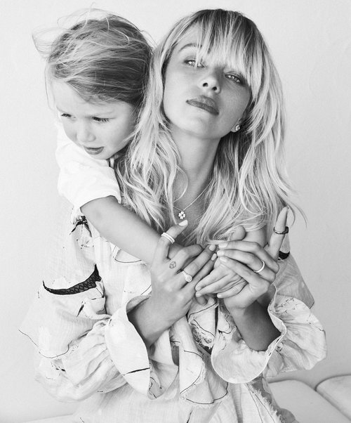Black and white portrait of a blonde woman in a patterned top holding a young child with light hair in an indoor setting.