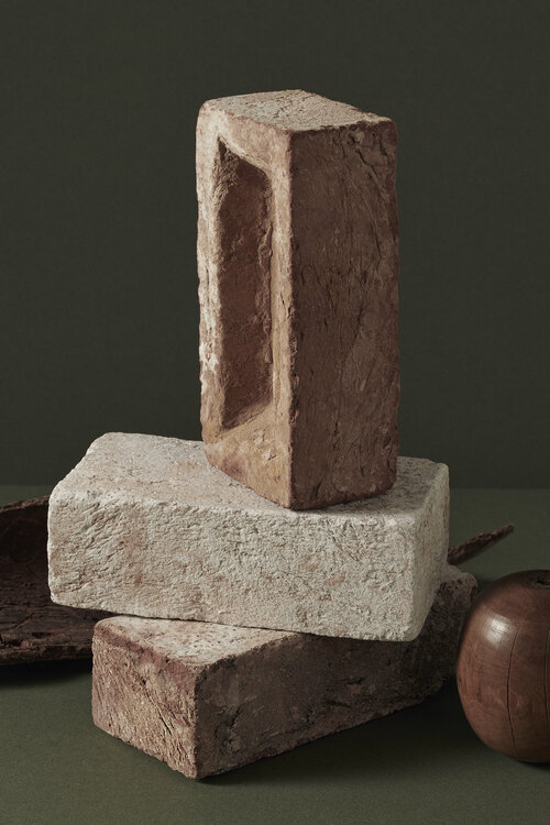 Still life of three stacked bricks in varying colors and textures against a muted olive green background, creating an architectural composition.