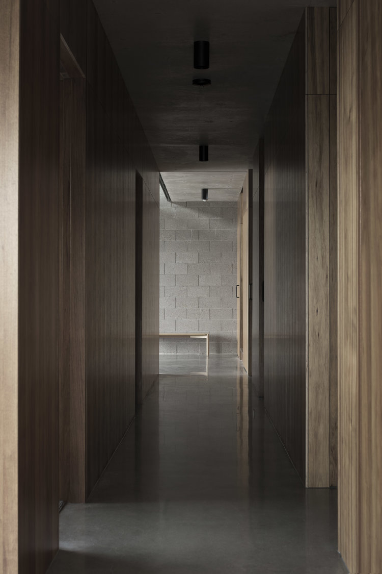 Interior hallway featuring light wood paneling, a grey concrete floor and ceiling, and recessed lighting, creating a modern design.