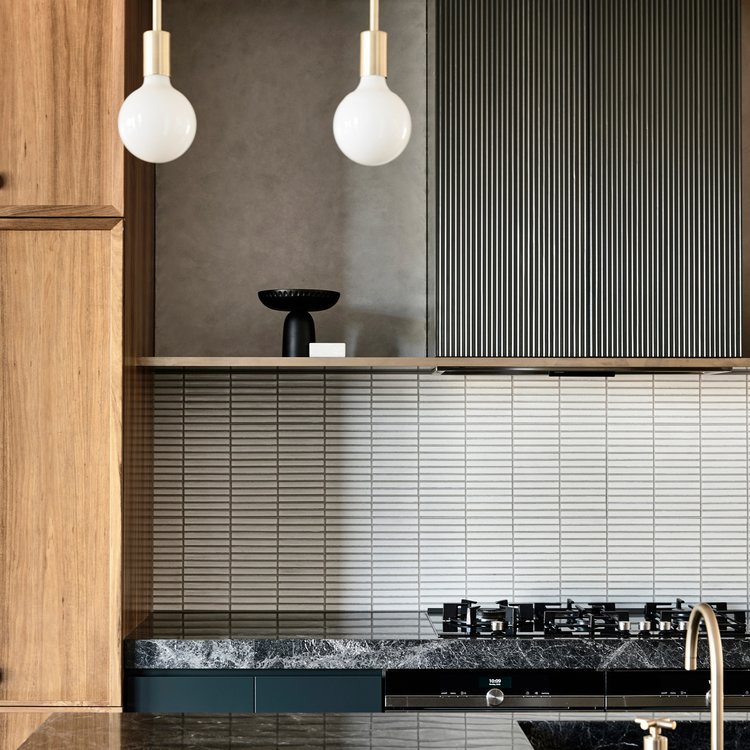 Modern kitchen interior featuring wood cabinets, a marble countertop, and pendant lights hanging from the ceiling, indoor shot.