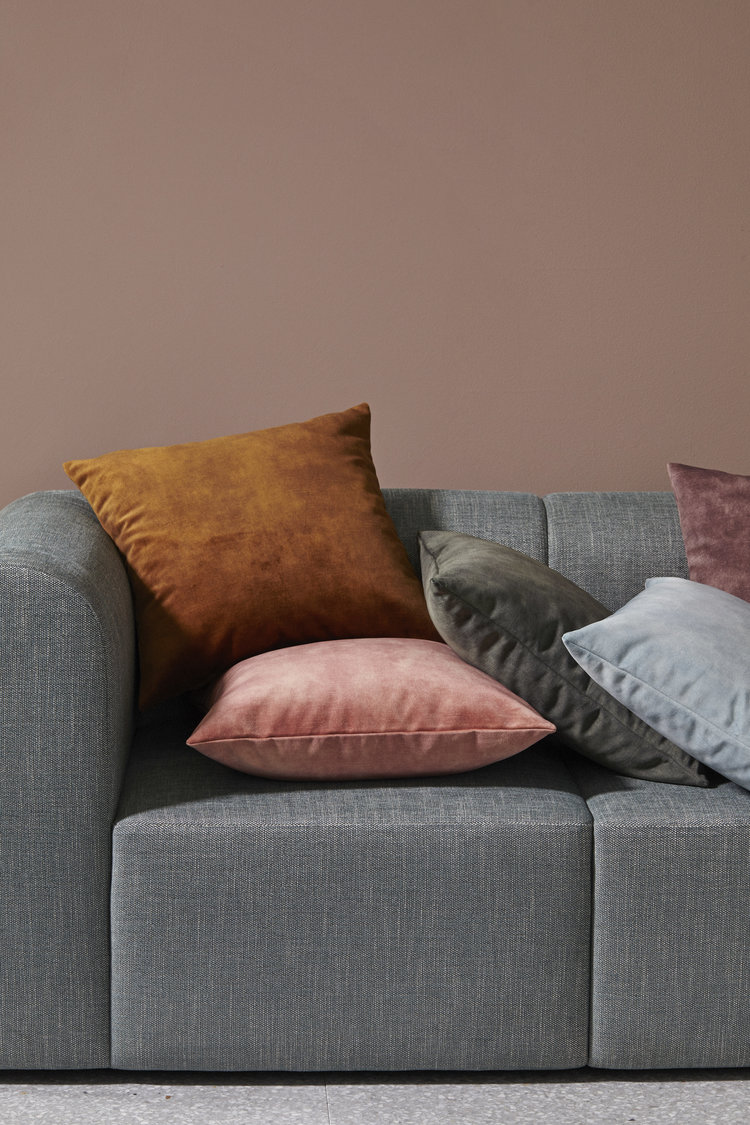 Grey couch with a collection of decorative pillows in shades of brown, pink, grey, and blue, creating a cozy and inviting interior scene.