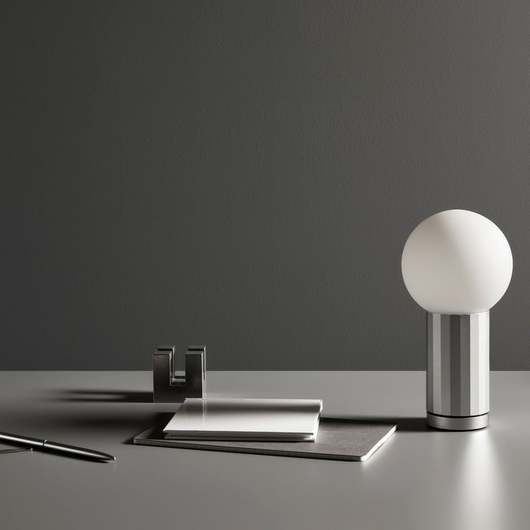 Still life of desk lamp, pen, notebook, and metal stationery holder against a grey background in a minimalist composition.