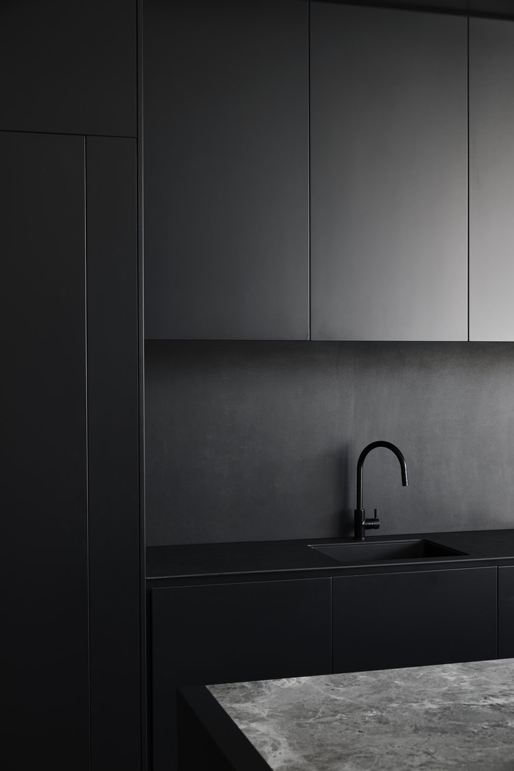 Modern kitchen interior featuring sleek, black cabinetry, black faucet and sink, and a gray marble countertop in a minimalist design.