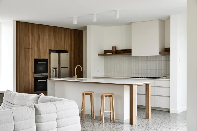 Modern kitchen interior featuring wood cabinets, stainless steel appliances, a white island with stools, and speckled flooring.