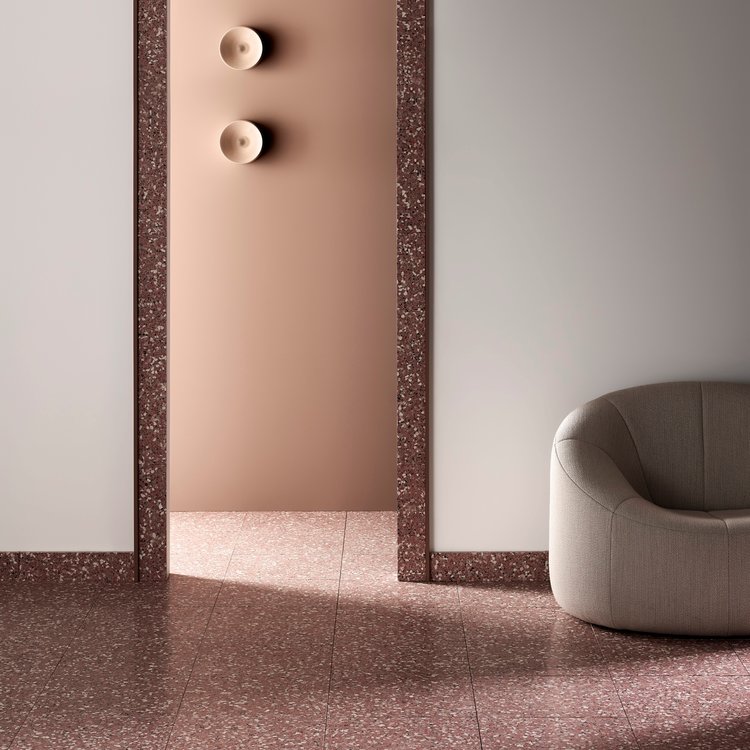 Beige armchair in a minimalist interior with salmon-colored walls, terrazzo flooring, and two gold wall sconces for interior design.