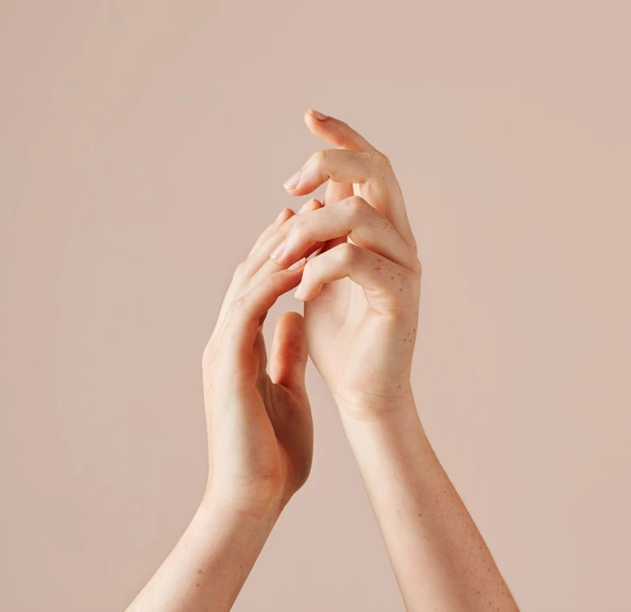 Close-up of two hands gently touching against a solid neutral beige background