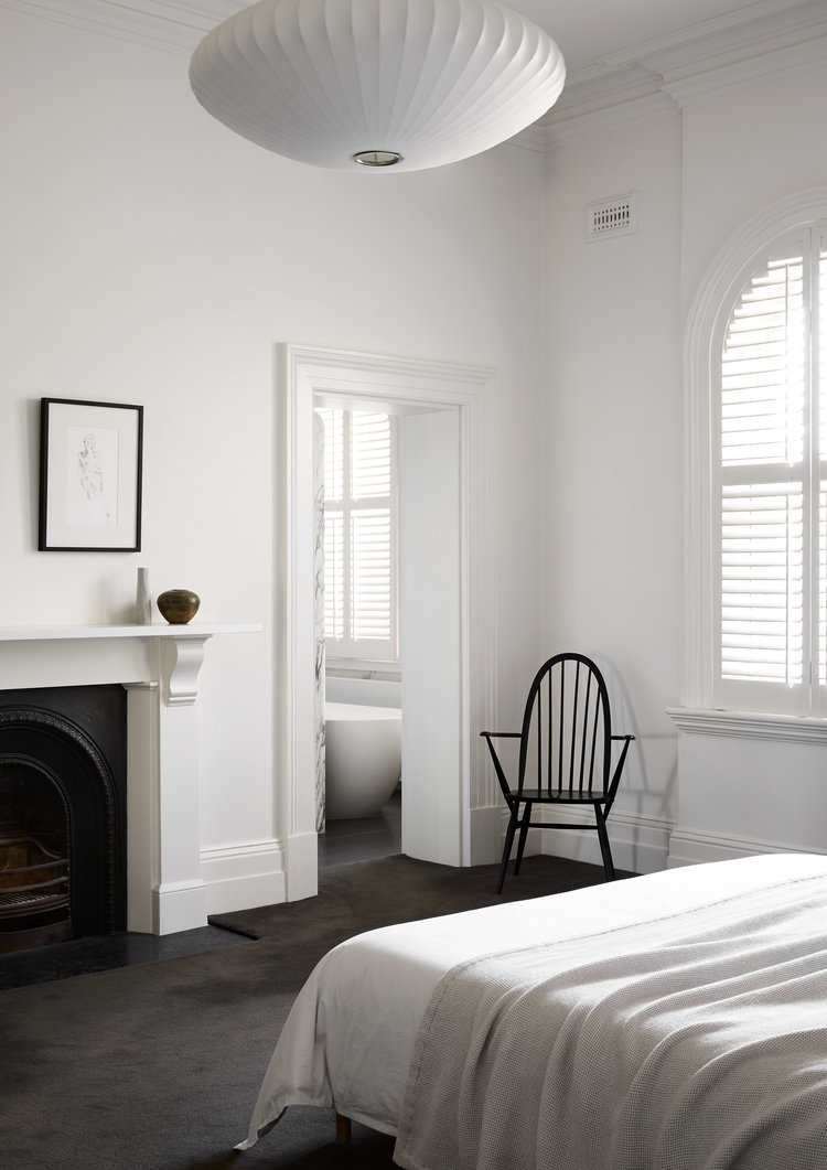Minimalist white bedroom interior styled by Bek Sheppard in Melbourne with a black Windsor chair and arched window shutters