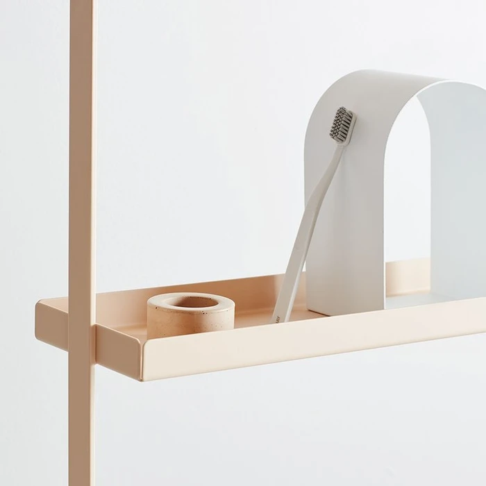 Minimalist interior product styling featuring a toothbrush and small container on a pale peach metal shelf.