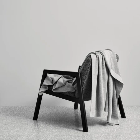 Black armchair with a draped grey knit blanket against a plain grey wall and speckled floor