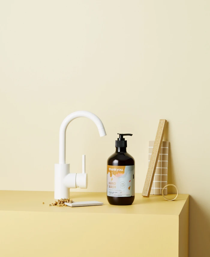 Dark amber hand wash bottle beside a white faucet on a yellow surface with a small wooden block and ceramic dish.