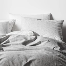 Close-up interior styling of a neatly made bed with grey textured pillows and a patterned duvet cover.