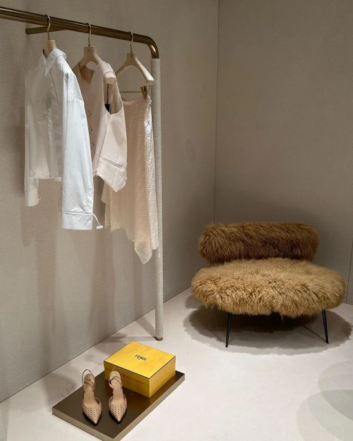 Display of curated fashion items: white shirt and cream skirt on a rack with shoes, box, and a shaggy chair in a retail setting.